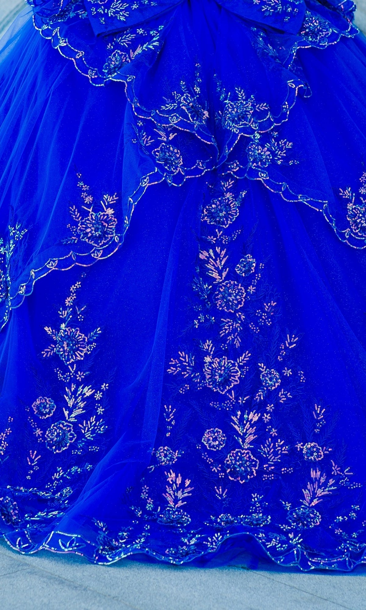 Close-up of the Quinceanera Ball Gown 8100J in royal blue, featuring off-the-shoulder style, sheer layers, iridescent beads, silver floral embroidery on the skirt, and a lace-up back for a perfect fit.